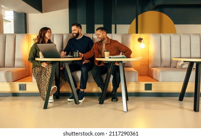 Modern entrepreneurs working together in a lobby. Team of happy businesspeople smiling while having a discussion. Group of entrepreneurs collaborating on a new project in a co-working space. - Shutterstock ID 2117290361