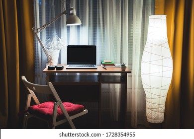 Modern Evening Interior Of Living Room With Small Office Desk And Floor Lamp Against  Window. Laptop On Table Ready To Start Late Night Work Overtime. Working From Home Concept