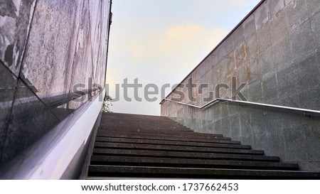 The modern exit from the pedestrian tunnel is empty, up the stairs. Staircase up to the street from the underpass. Stainless steel.