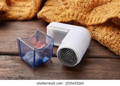 Modern fabric shaver with fuzz and orange knitted sweater on wooden table, closeup - Shutterstock ID 2255419265