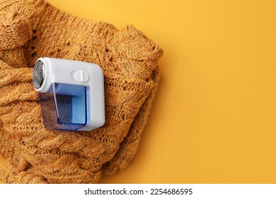 Modern fabric shaver and knitted sweater on orange background, top view. Space for text - Shutterstock ID 2254686595