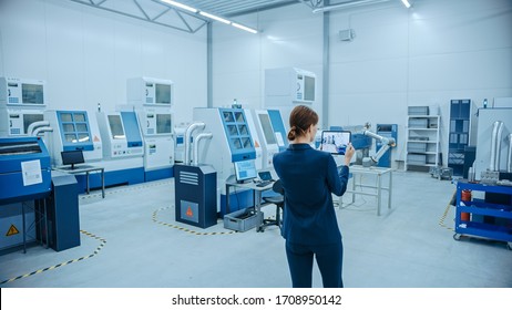 Modern Factory: Female Engineer Uses Digital Tablet Computer With Augmented Reality Software To Visualize Workshop For Room Mapping, Floor Layout. Facility With High-Tech CNC Machinery And Robot Arm