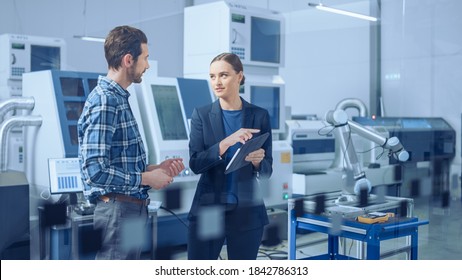 Modern Factory: Female Project Manager and Male Engineer Standing, Talking, Using Digital Tablet for Programming and Monitoring Assembly Line. Industry 4.0 Facility with High-Tech CNC Machinery - Powered by Shutterstock