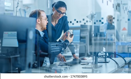 Modern Factory: Female Project Supervisor Talks To A Male Industrial Engineer Who Works On Computer. They Inspect Machinery Mechanism And Design Improved Version. Working High-Tech Industrial Facility