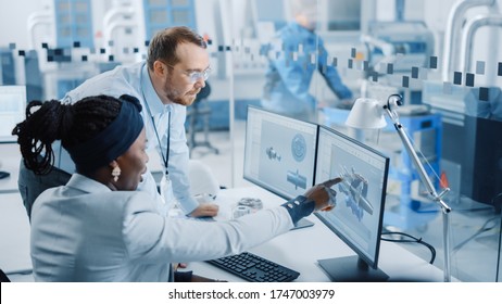 Modern Factory: Male Project Supervisor Talks to a Female Industrial Engineer who Works on Computer. They use CAD Software for Design Hybrid Electric Engine. Working High-Tech Industrial Facility