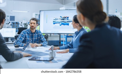 Modern Factory Office Meeting Room: Diverse Team Of Engineers, Managers And Investors Talking At Conference Table, Use Interactive TV, Analyze Sustainable Energy Engine Blueprints. High-Tech Facility