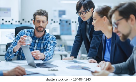 Modern Factory Office Meeting Room: Multi-Ethnic and Diverse Team of Engineers, Managers and Investors Talking Sitting at Conference Table, Analyzing Blueprints, Showing Information on Laptop Computer - Powered by Shutterstock