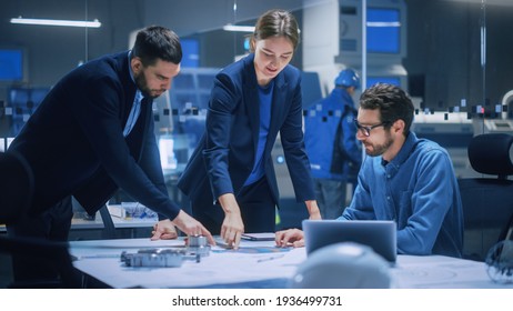Modern Factory Office Meeting Room: Diverse Team of Engineers, Managers Talking at Conference Table, Look at Blueprints, Inspect Mechanism, Use Laptop. High-Tech Facility with CNC Machines