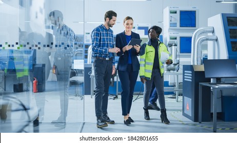 Modern Factory: Project Manager, Engineer, Worker Walk Through High Tech Development Facility, Talking And Using Tablet Computer. High-Tech Facility With CNC Machinery, Robot Arm Production Line