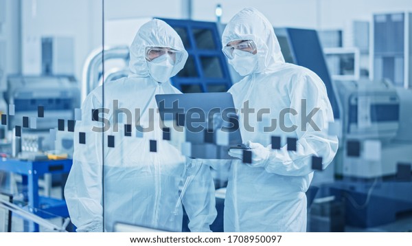 Modern Factory Sterile Workshop: Professionals\
in Coveralls, Masks Use Laptop and Talk. Medical Manufacturing\
Laboratory with High Tech CNC Machinery, Robot Arm Production Line\
and Automatic Equipment