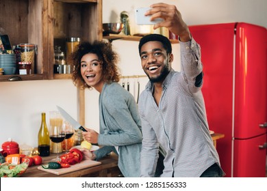 Modern family lifestyle. Happy young african-american couple in kitchen taking selfie on smarphone, preparing healthy food. - Powered by Shutterstock