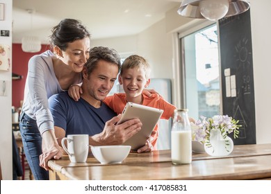 A modern family using a digital tablet while having breakfast in the kitchen, mom,  dad and their eight year old son - Powered by Shutterstock