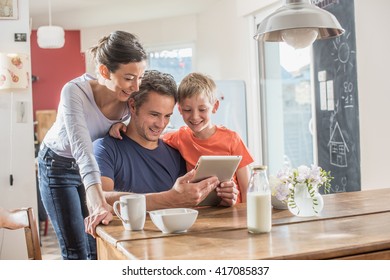 Eine moderne Familie, die eine digitale Tablette benutzt, während sie in der Küche frühstückt, Mutter, Vater und ihr acht Jahre alter Sohn.  Sie tragen ungezwungene Kleidung