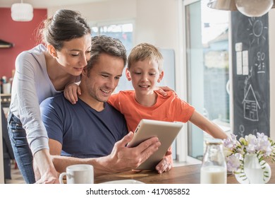 A modern family using a digital tablet while having breakfast in the kitchen, mom,  dad and their eight year old son. They are wearing casual clothes