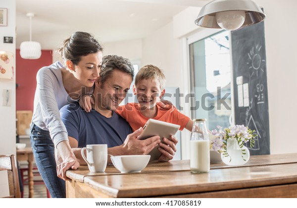 A modern\
family using a digital tablet while having breakfast in the\
kitchen, mom,  dad and their eight year old\
son