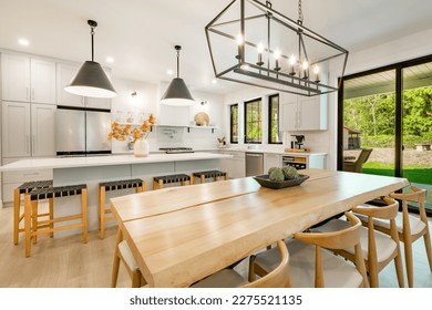 Modern farmhouse kitchen interior with light wood floors white granite marble counters large dining table with eight chairs stainless appliances orange color accents and large windows with black trim - Shutterstock ID 2275521135
