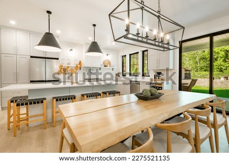 Modern farmhouse kitchen interior with light wood floors white granite marble counters large dining table with eight chairs stainless appliances orange color accents and large windows with black trim