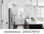 A modern farmhouse kitchen with white cabinets and a black island, stainless steel appliances, apron sink, and dark hardwood floors. No brands or labels.