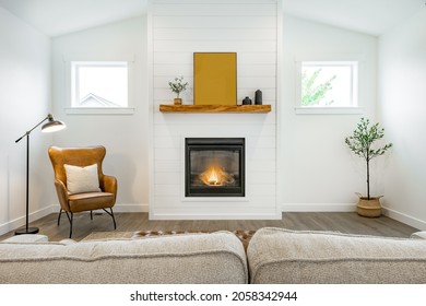 Modern farmhouse simple living room with minimal decor gas fireplace with a raw edge wooden mantel brown leather armchair and sofa