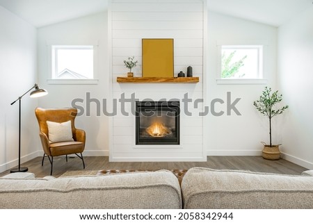 Modern farmhouse simple living room with minimal decor gas fireplace with a raw edge wooden mantel brown leather armchair and sofa