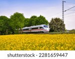 Modern fast train passing a yellow blooming rapeseed field on the main railway track between Dortmund, Bochum and Essen in Ruhrbasin Germany. Colorful landscape on a sunny springtime day.