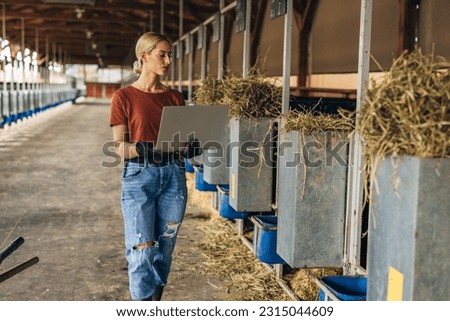 Modern female farmer using laptop in a stable.