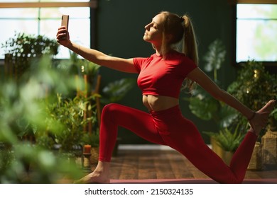 Modern Female In Red Fitness Clothes With Smartphone Doing Yoga And Having Virtual Meeting At Modern Green Home.