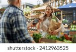 Modern Female Shopper Using Smartphone with Contactless Payment Technology to Pay for Organic Vegetables at a Farmers Market. Street Vendor Holding an Electronic Online Payment Terminal Device