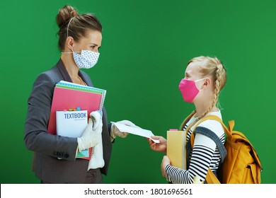 modern female teacher and pupil with masks, medical certificate on covid testing result, yellow backpack and textbook isolated on chalkboard green.