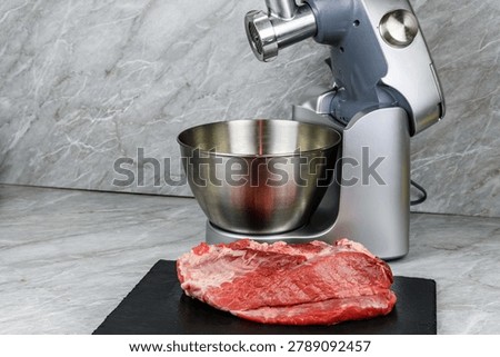 Modern food processor with meat grinder and peace of pork meat on kitchen table