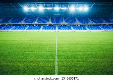 Modern Football Stadium In The Evening. Soccer Arena, Background. Green Grass, Blue Seats