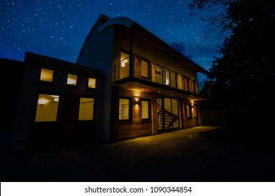 Modern Four Bedroom Detached Family Home At Night With The Lights On. 