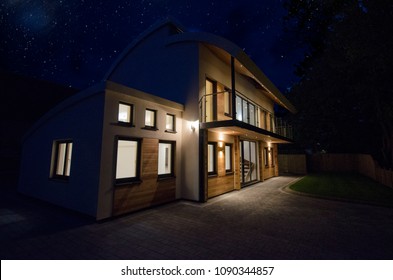 Modern Four Bedroom Detached Family Home At Night With The Lights On. 