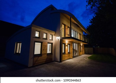 Modern Four Bedroom Detached Family Home At Night With The Lights On. 