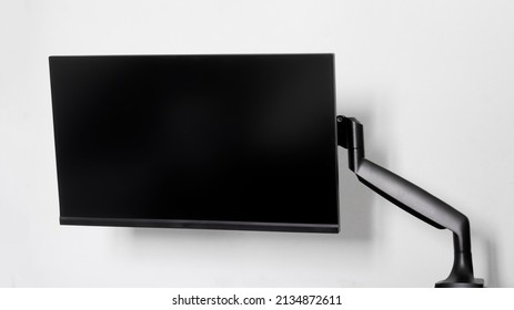 A modern frameless thin computer monitor or TV is mounted on a metal swivel desktop bracket with a gas lift function. Off-center side holder. Form. Copy space. Light background