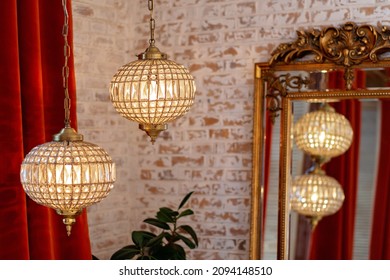 Modern French Interior With Corduroy Burgundy Curtains, Vintage Gold Mirror And Crystal Chandeliers Against A Brick Wall. Soft Selective Focus.