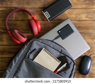 Modern gadgets and gray textile backpack or bag on wooden table. Laptop, portable ssd, smartphone, notepad, pen, headphones, mouse and external battery - poverbank. For work and study. Close-up