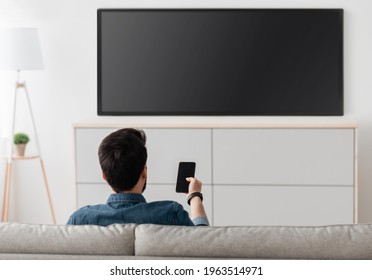 Modern Gadgets. Unrecognizable Man With Smartphone Connected To TV, Watching Video At Home, Back View. Guy Transfering Video From Phone To Television. Information Transfer Between Devices Over Wifi.