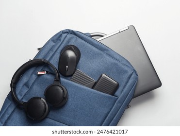 Modern gadgets For work and study. Backpack with laptop, headphones, external hard drive, pc mouse and power bank on white background. Top view. Flat lay