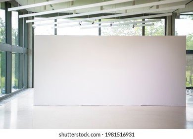 Modern Gallery Interior With Blank White Empty Canvas. Contemporary, Open Space, City View And Daylight. Marble Floor. Green Trees In Background. Light Spots,generic Design Furniture And Building.