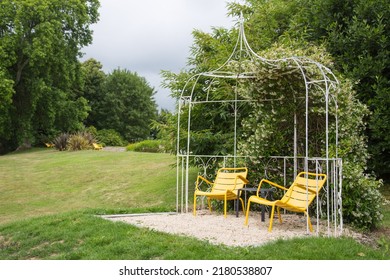 Modern garden design and landscaping: Recreation area in a garden on a hillside plot, idyllic resting place with two yellow chairs under an iron weatherproof pavilion 