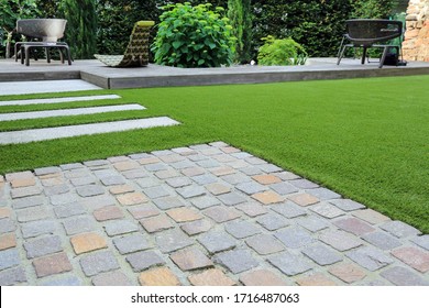 Modern Garden Design And Terrace Construction With A Material Mix Of Cobble Paving Stones And Concrete Paving Slab And Artificial Lawn And Wood