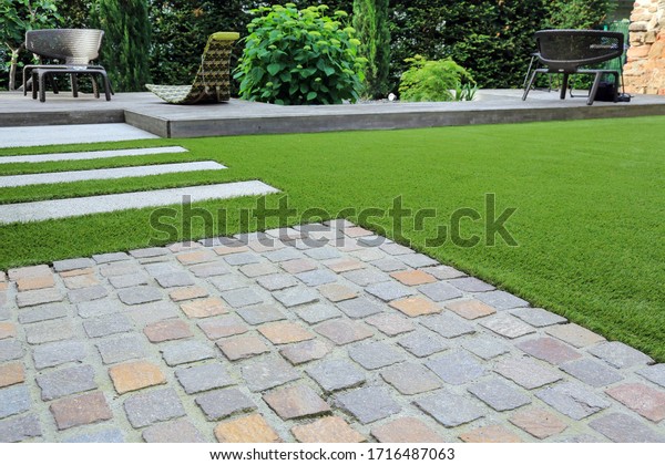 Modern garden design and terrace construction\
with a material mix of cobble paving stones and concrete paving\
slab and artificial lawn and\
wood