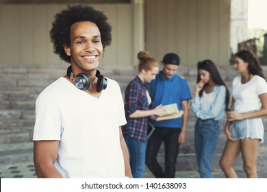 Modern Generation. Friendly African American Teen Guy Smiling At Camera, His Friends Talking On Background, Free Space