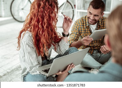 Modern generation. Joyful red haired woman holding a laptop while talking with her colleagues