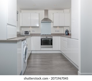 A Modern Generic New Build Kitchen With Built In Units And Oven With Aluminium Cooker Hood.
Finished In High Gloss White With Under Cabinet Lights And Grey Laminate Link Flooring.