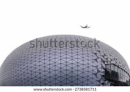 Modern geodesic dome stadium with triangular metal panels and geometric pattern, airplane flying overhead against cloudy sky in Hong Kong