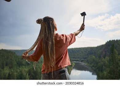 a modern girl with dreadlocks records her blog standing with her back to the camera on top of a cliff overlooking the river and dense forest. High quality photo - Powered by Shutterstock