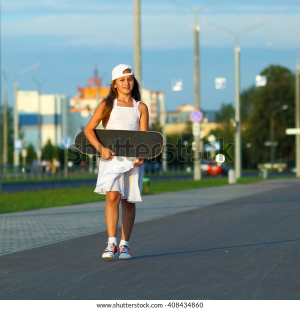 Modern Girl teenager with a skateboard at sunset\
on a city street