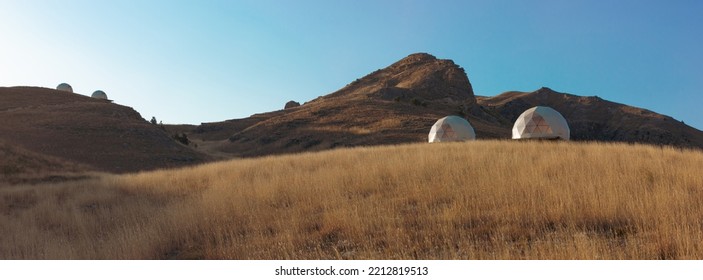 Modern Glamorous Camping In The Autumn Mountains Of Dagestan. A Group Of Futuristic Hotel Geodesic Domes Tents In The Middle Of A Dry Grass Meadow In The Khunzakh Region.